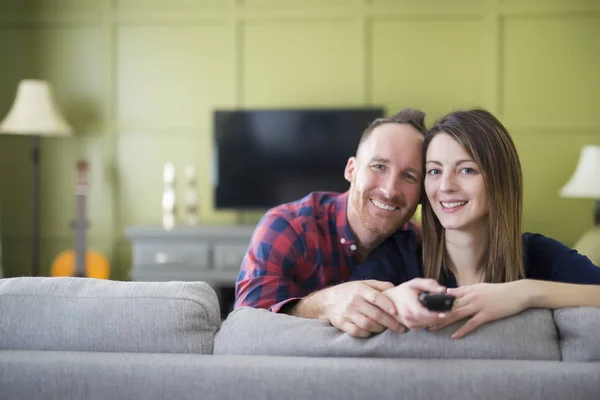 Beautiful couple watching TV sitting on couch at home — Stock Photo, Image