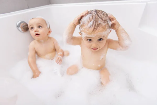Два маленьких мальчика развлекаются с водой, принимая ванну в ванной — стоковое фото