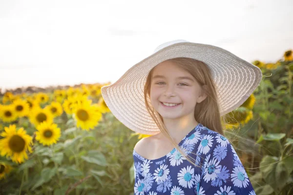 Glad tjej på ett fält av solrosor på sommar solnedgång — Stockfoto