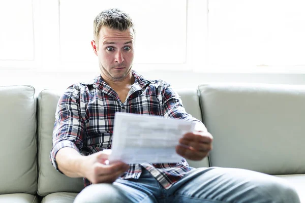 Geschokt man met bepaalde documenten op sofa woonkamer — Stockfoto