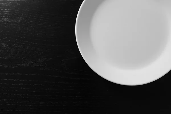 Empty white plate on black wooden table — Stock Photo, Image