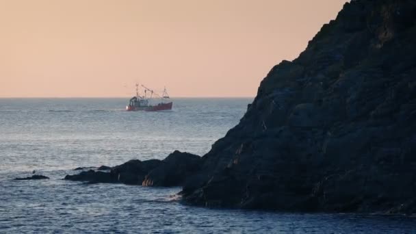 夕暮れ時の岩の後ろに釣り船のパス — ストック動画