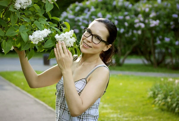 Beautiful young girl smiling in a park with flowers of lilac — Stock Photo, Image