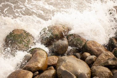 Deniz taşlara çarpıyor ve su sıçrıyor.