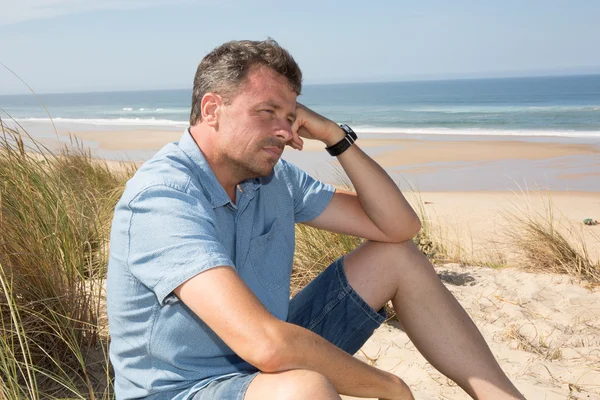 Handsome and confident man smiling and sitting at the beach — Stock Photo, Image