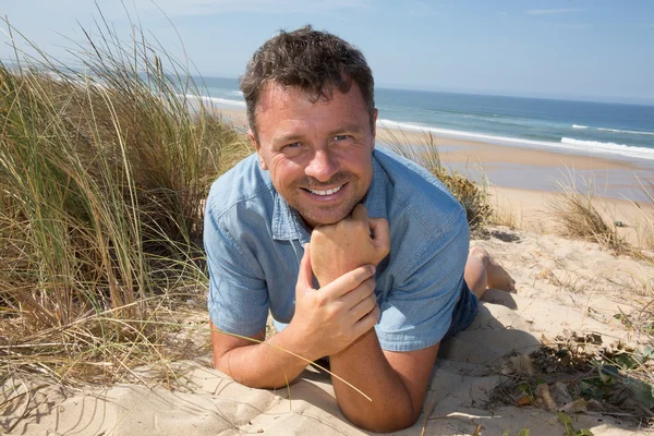 Sorridente bell'uomo che si rilassa sulla spiaggia sdraiato sulla sabbia — Foto Stock