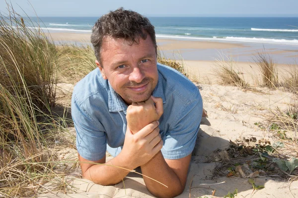 Sorridente bell'uomo che si rilassa sulla spiaggia sdraiato sulla sabbia — Foto Stock