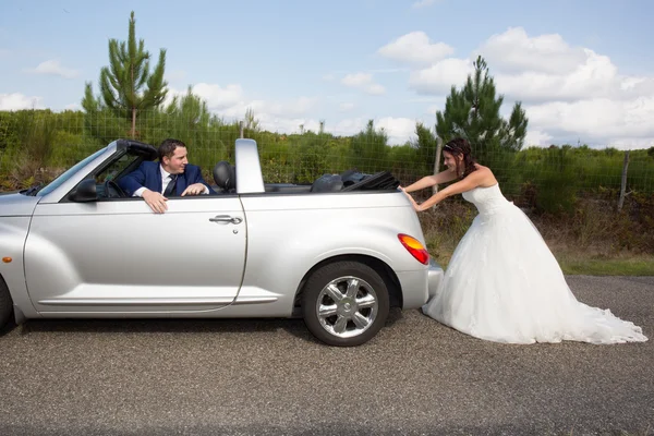 Красивый жених сидит в кабриолете, пока невеста толкает его — стоковое фото