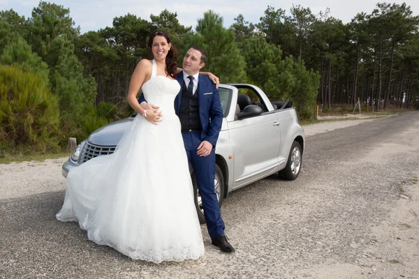 Lovely cute groom and bride on a grey convertible car posing — Stock Photo, Image