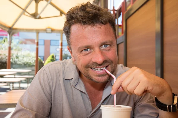 Smiling man drinking a frozen beverage at restaurant — Stock Photo, Image