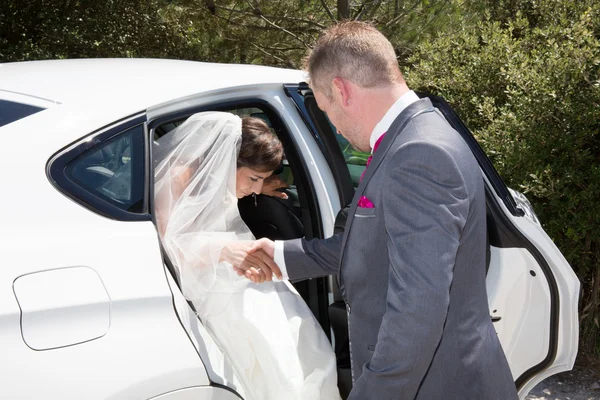 Fröhlicher Bräutigam nimmt seine Braut aus dem Hochzeitsauto — Stockfoto