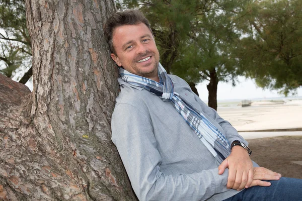 Smiling middle aged man relaxing In countryside leaning against tree — Stock Photo, Image