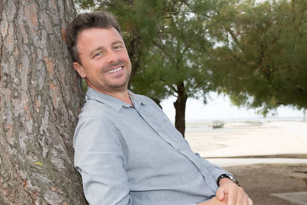 Middle aged man relaxing leaning against tree — Stock Photo, Image