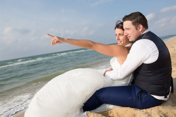 Новобрачная пара указывает на что-то на пляже — стоковое фото