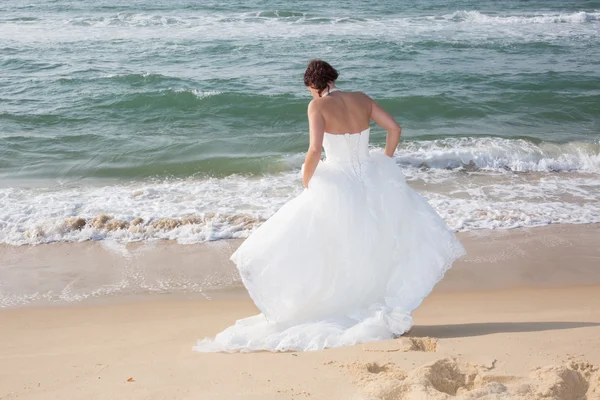 Novia caminando a lo largo de la costa del mar usando hermoso vestido de novia — Foto de Stock