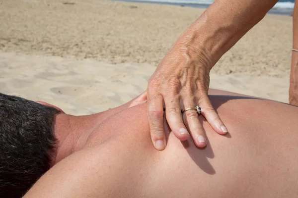Man op het strand krijgt een massage door vrouw — Stockfoto