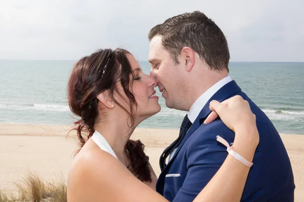 Leende bruden och brudgummen embracing på stranden — Stockfoto