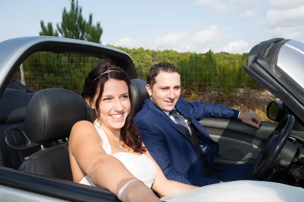 Cheerful bride and groom on their wedding car — Stock Photo, Image
