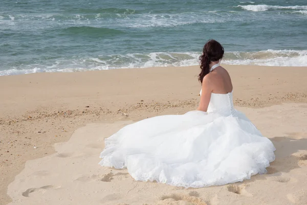 Невеста сидит на берегу моря в свадебном платье — стоковое фото