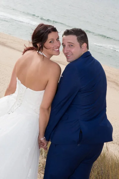Baksidan av glada par på stranden i brudklänning — Stockfoto