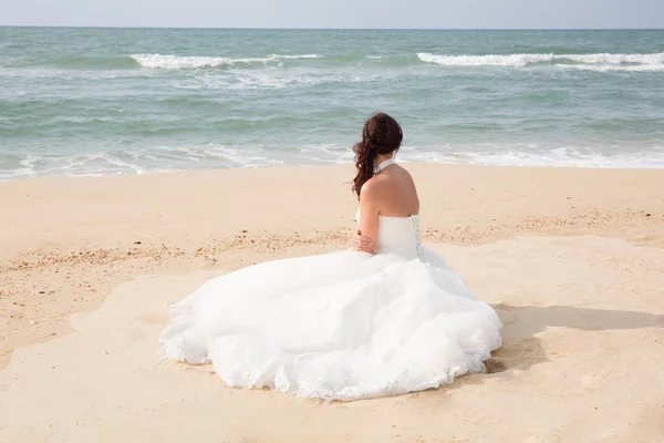Nevěsta sedí podél pobřeží moře ve svatebních šatech — Stock fotografie