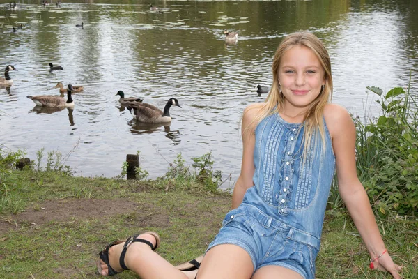 Uma menina feliz no parque perto da água com pássaros — Fotografia de Stock