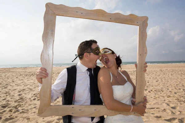 Mit venezianischer Maske spielt das Brautpaar am Strand — Stockfoto