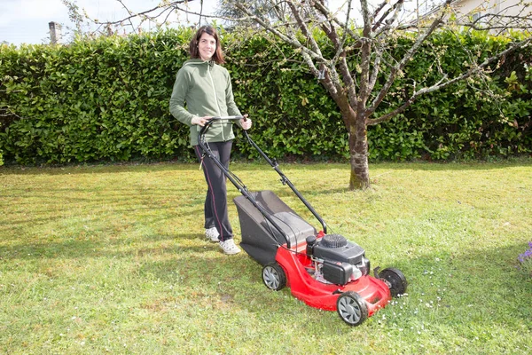 Mulher passa o cortador de grama no jardim da família — Fotografia de Stock