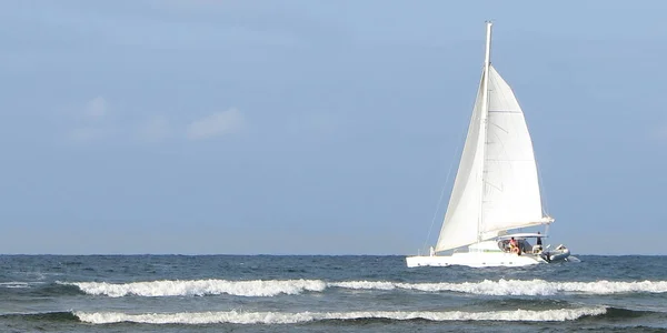 Vista da praia ou um barco passa sobre o horizonte com suas velas no vento — Fotografia de Stock