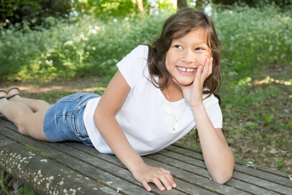 Ganska ung flicka liggande på bänk park i sommar — Stockfoto