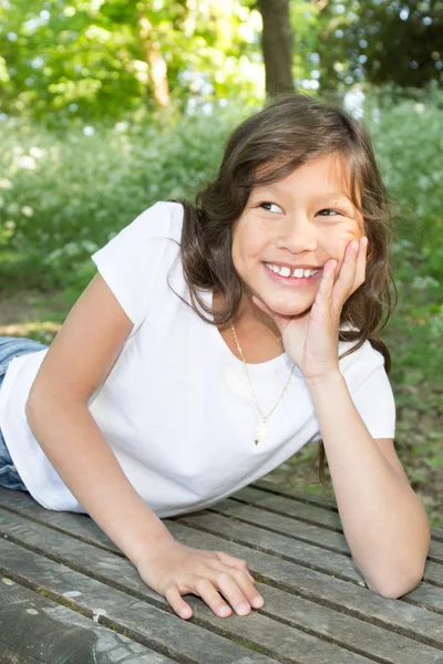 Muito jovem misturado menina com cabelos cacheados deitado no banco parque no verão — Fotografia de Stock