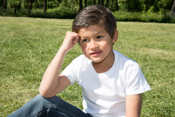 Mladý chlapec sedí v trávě v parku — Stock fotografie