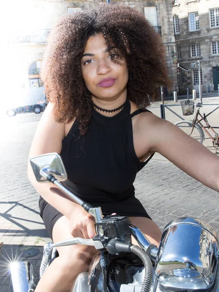beautiful young woman with curly hair in a black dress on a motorcycle