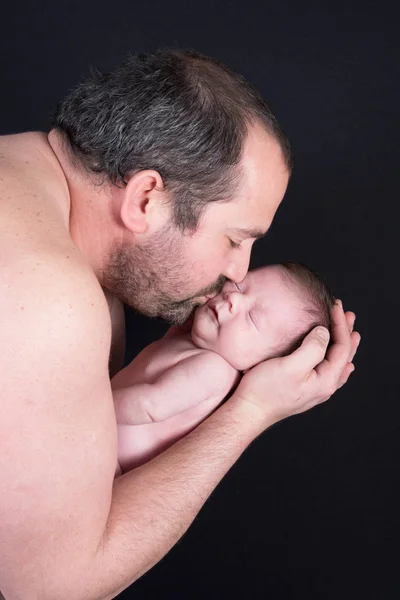 Beautiful newborn baby kissing father with a black background — Stock Photo, Image