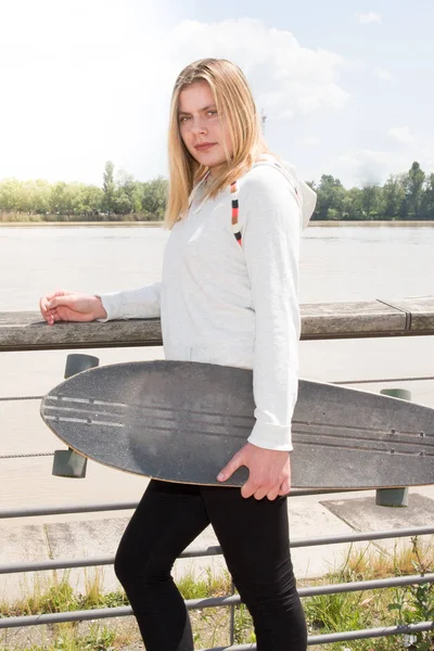 Szőke lány gördeszka longboard City közelében folyó — Stock Fotó