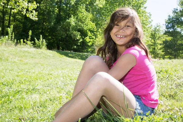 Girl with long hair sitting in grass in pink t-shirt — Stock Photo, Image