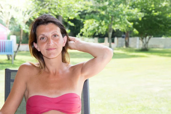 Bella giovane donna seduta su una sedia nel suo giardino durante l'estate — Foto Stock