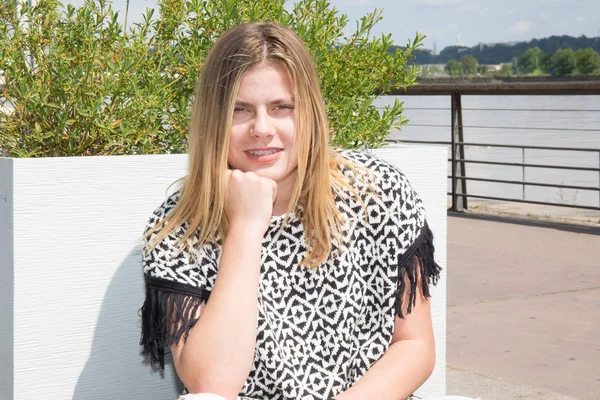 Chica rubia adolescente sentada junto al río en la ciudad —  Fotos de Stock