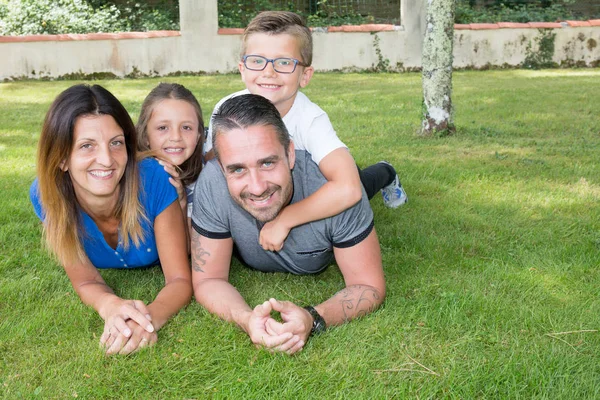 Família feliz 4 pessoas deitadas na grama com um menino e uma menina — Fotografia de Stock