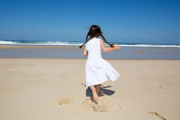 Bakifrån lilla flicka kör i sandstrand med vit klänning — Stockfoto