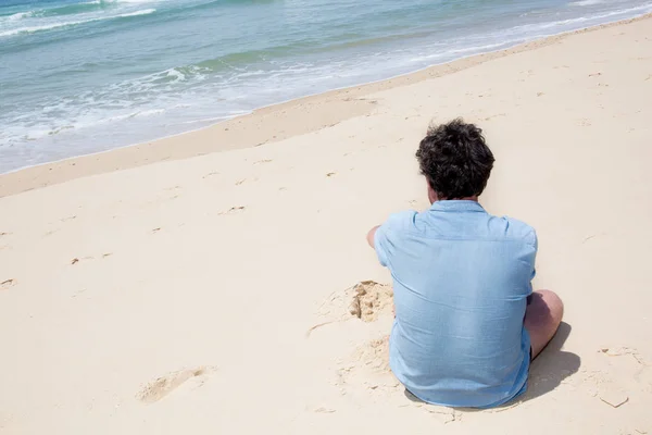 Solo uomo seduto sulla sabbia sulla spiaggia — Foto Stock