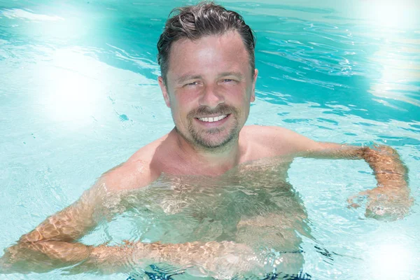 handsome man in the pool enjoys the relaxation and sun