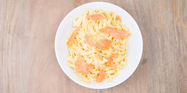 fresh pasta with salmon in a white plate at top view