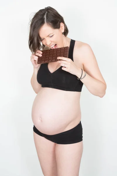 立っている妊娠中の女性の肖像画の腹を見て チョコレートを食べる — ストック写真
