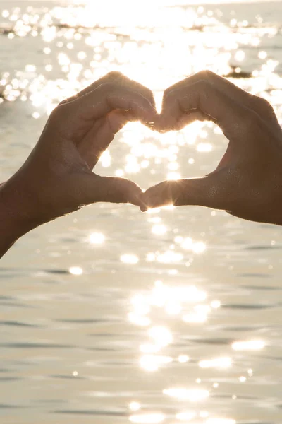 Female hands in the form of heart against the water sea sunset