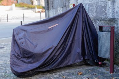 Caddedeki motosiklet koruma altında. Motosiklet brandası ceketiyle korunuyor.