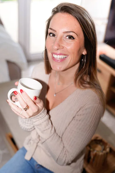 Happy woman holding tea mug coffee cup in winter at home