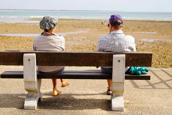 上了年纪的退休夫妇坐在长椅上 在低潮中眺望着大西洋的海滨 — 图库照片