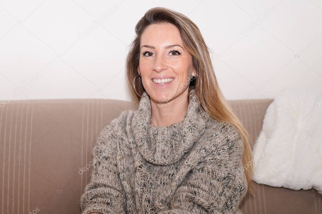 Smiling young beautiful blonde woman sit on home couch