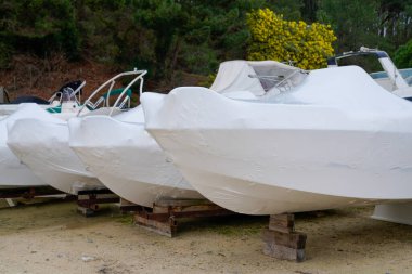 motorlu tekne park yeri beyaz koruyucu plastik film kaplamalı yeni modern tekneler soğuk kış mevsimi için depolanan yelkenlinin ambalajında muhafaza ediliyor